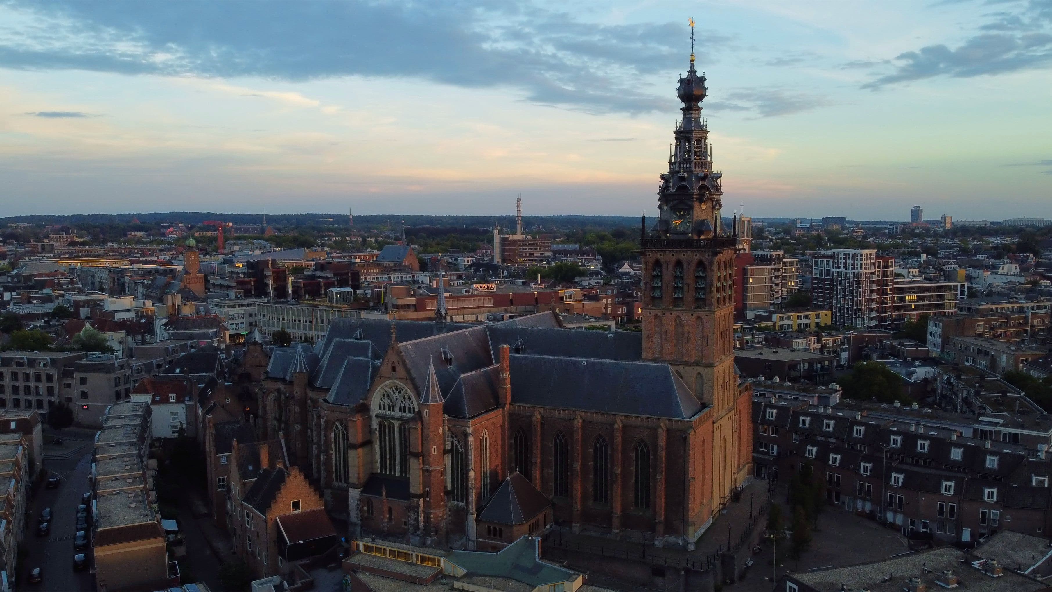 Het centrum van Nijmegen in de avondschemering, gezien vanuit de lucht, met de Stevenskerk en haar toren boven de daken uit.